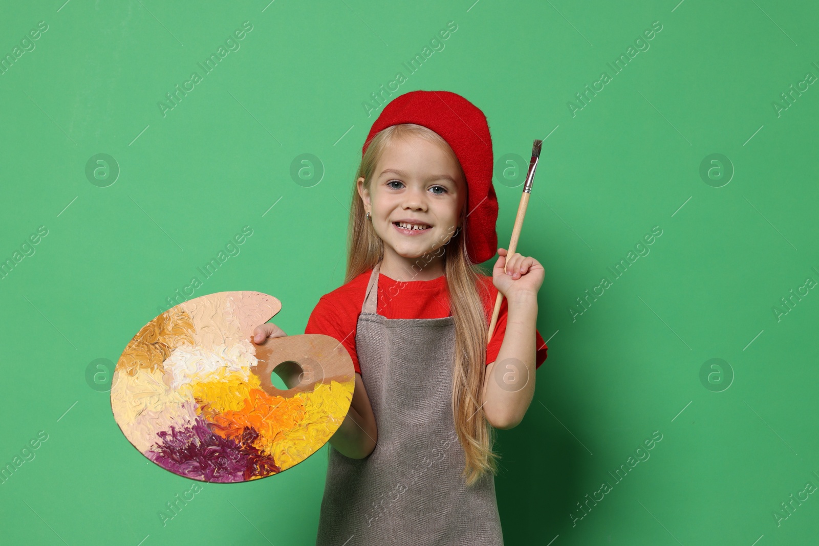 Photo of Little girl with brush and palette pretending to be artist on green background. Dreaming of future profession