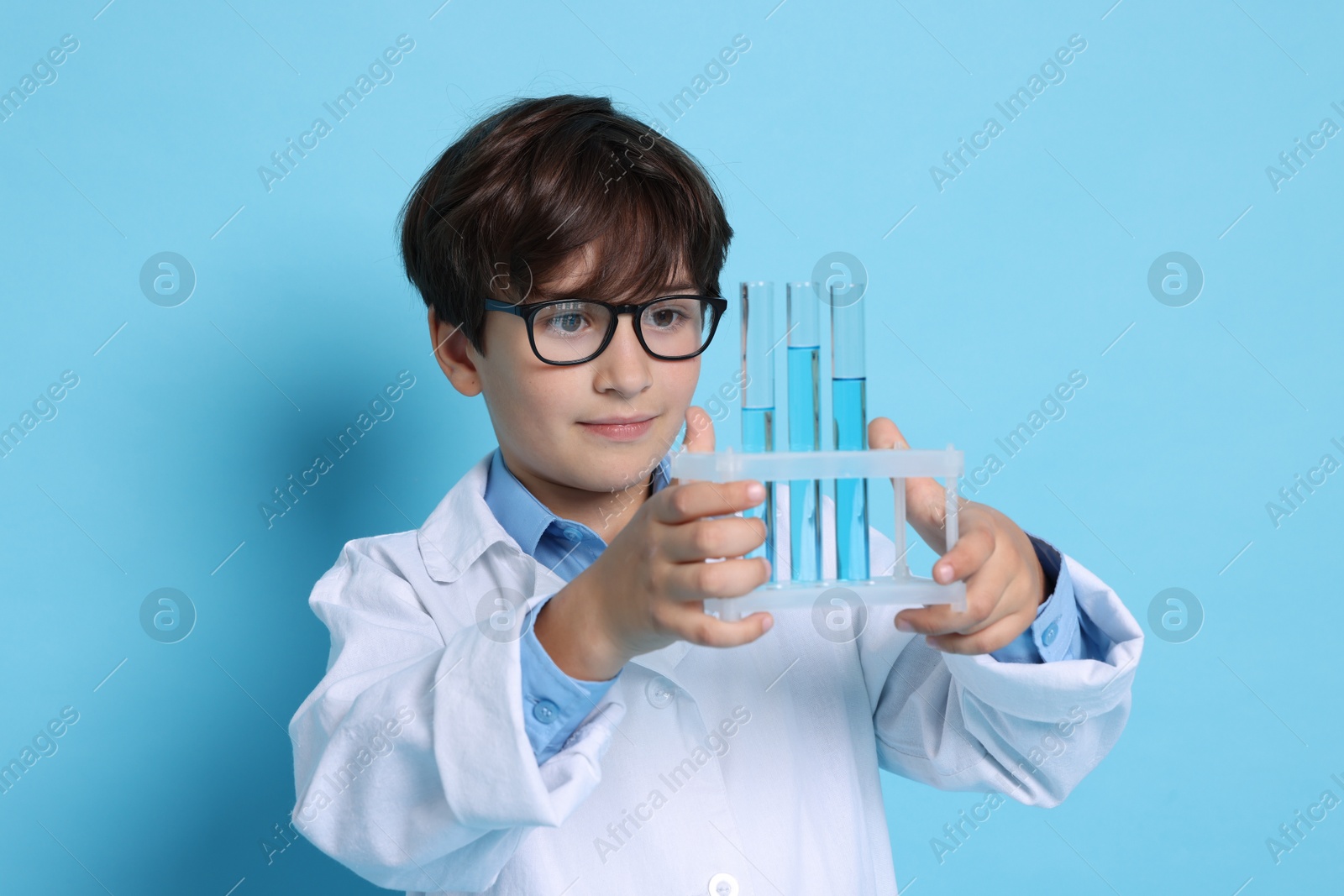 Photo of Boy with test tubes pretending to be scientist on light blue background. Dreaming of future profession