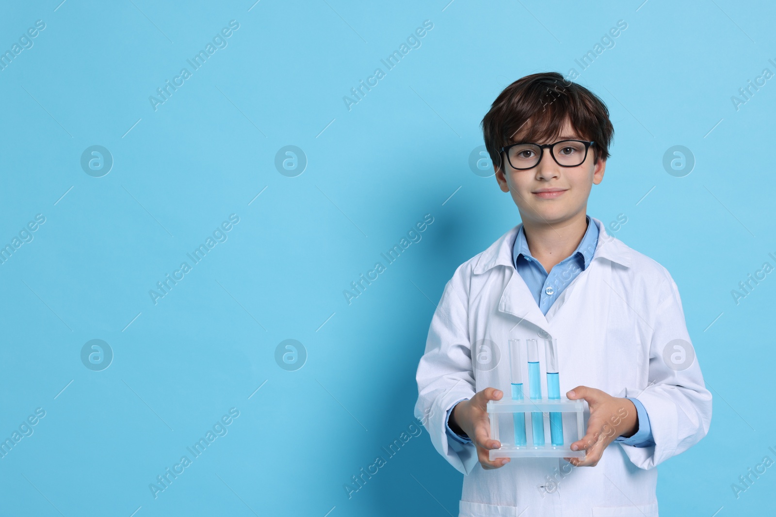 Photo of Boy with test tubes pretending to be scientist on light blue background, space for text. Dreaming of future profession