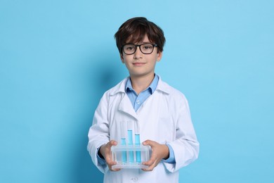 Photo of Boy with test tubes pretending to be scientist on light blue background. Dreaming of future profession