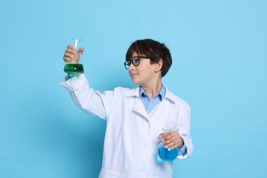 Photo of Boy with glassware pretending to be scientist on light blue background. Dreaming of future profession