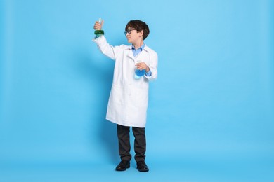 Boy with glassware pretending to be scientist on light blue background. Dreaming of future profession