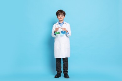 Boy with glassware pretending to be scientist on light blue background. Dreaming of future profession