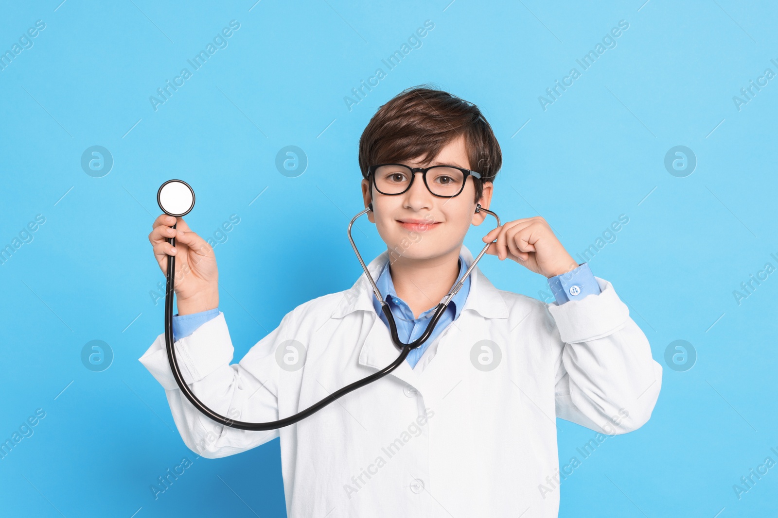 Photo of Boy with stethoscope pretending to be doctor on light blue background. Dreaming of future profession