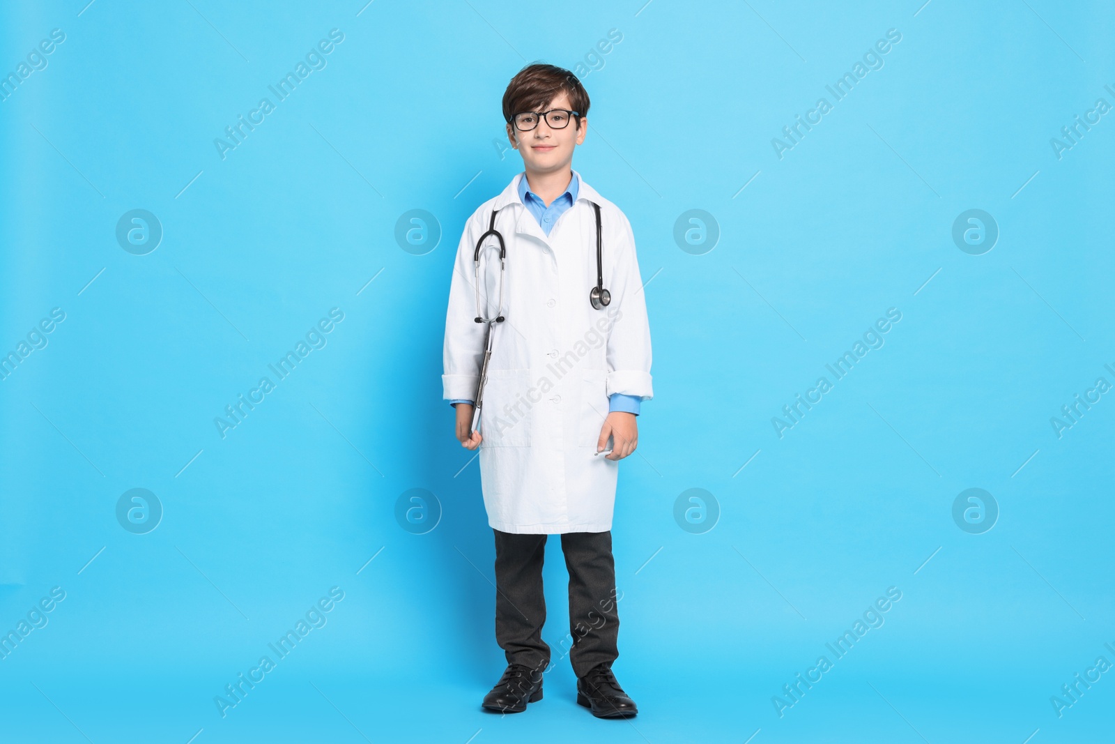 Photo of Boy with stethoscope pretending to be doctor on light blue background. Dreaming of future profession