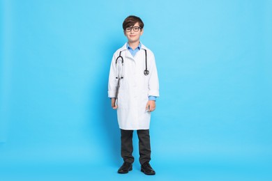 Boy with stethoscope pretending to be doctor on light blue background. Dreaming of future profession