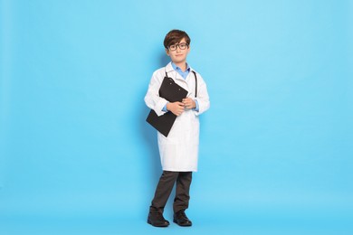 Boy with stethoscope and clipboard pretending to be doctor on light blue background. Dreaming of future profession