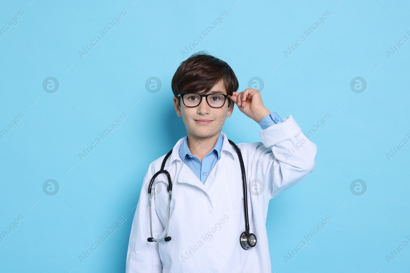 Photo of Boy with stethoscope pretending to be doctor on light blue background. Dreaming of future profession