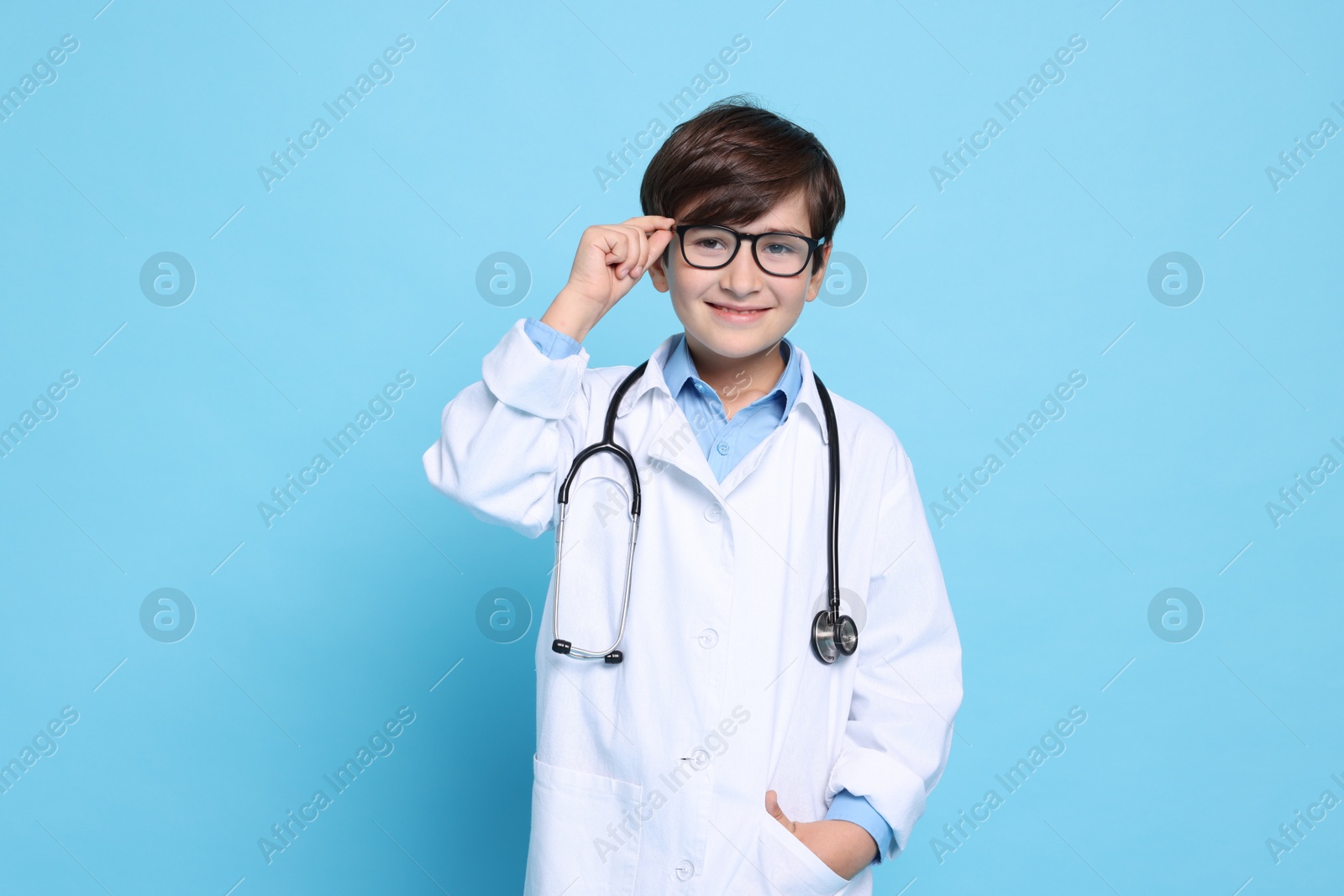 Photo of Boy with stethoscope pretending to be doctor on light blue background. Dreaming of future profession