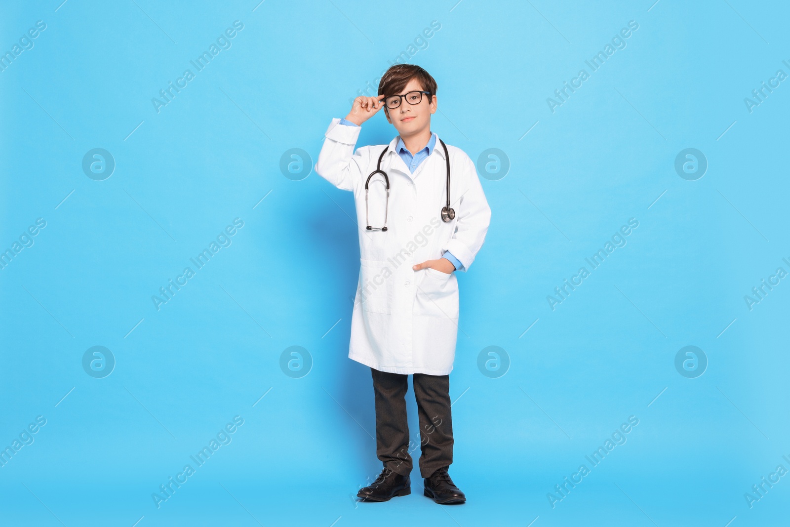 Photo of Boy with stethoscope pretending to be doctor on light blue background. Dreaming of future profession