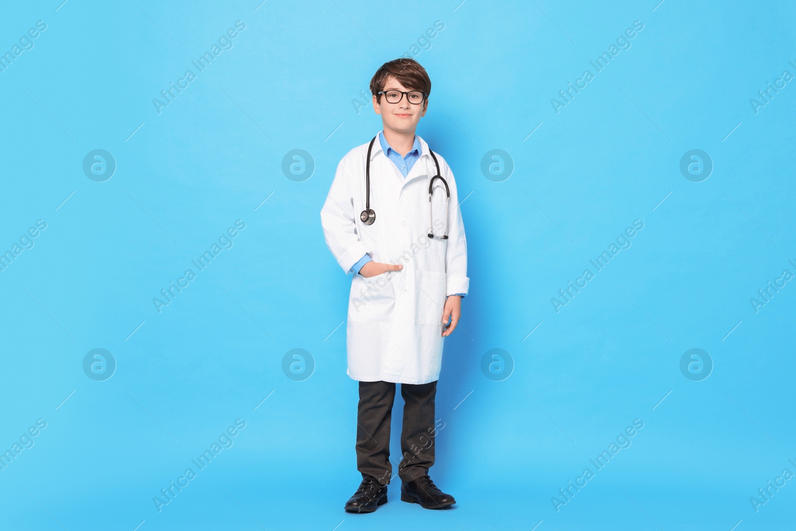 Photo of Boy with stethoscope pretending to be doctor on light blue background. Dreaming of future profession