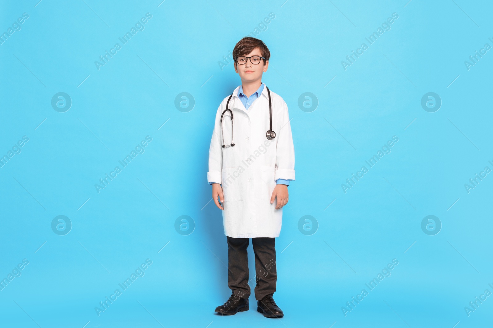 Photo of Boy with stethoscope pretending to be doctor on light blue background. Dreaming of future profession