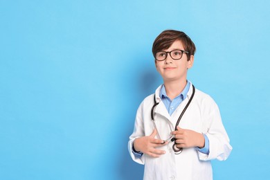 Photo of Boy with stethoscope pretending to be doctor on light blue background, space for text. Dreaming of future profession