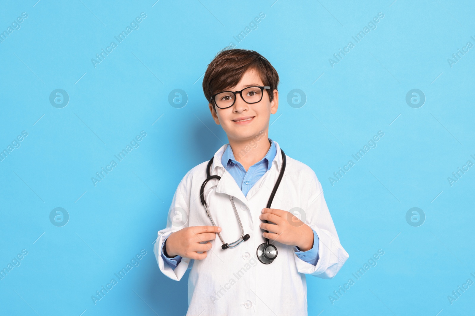 Photo of Boy with stethoscope pretending to be doctor on light blue background. Dreaming of future profession