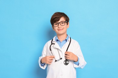 Boy with stethoscope pretending to be doctor on light blue background. Dreaming of future profession