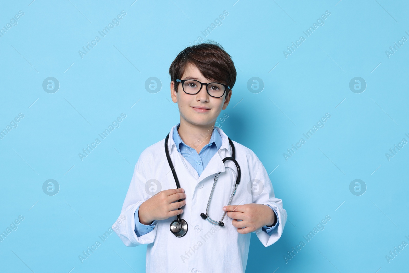 Photo of Boy with stethoscope pretending to be doctor on light blue background. Dreaming of future profession