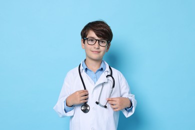 Photo of Boy with stethoscope pretending to be doctor on light blue background. Dreaming of future profession