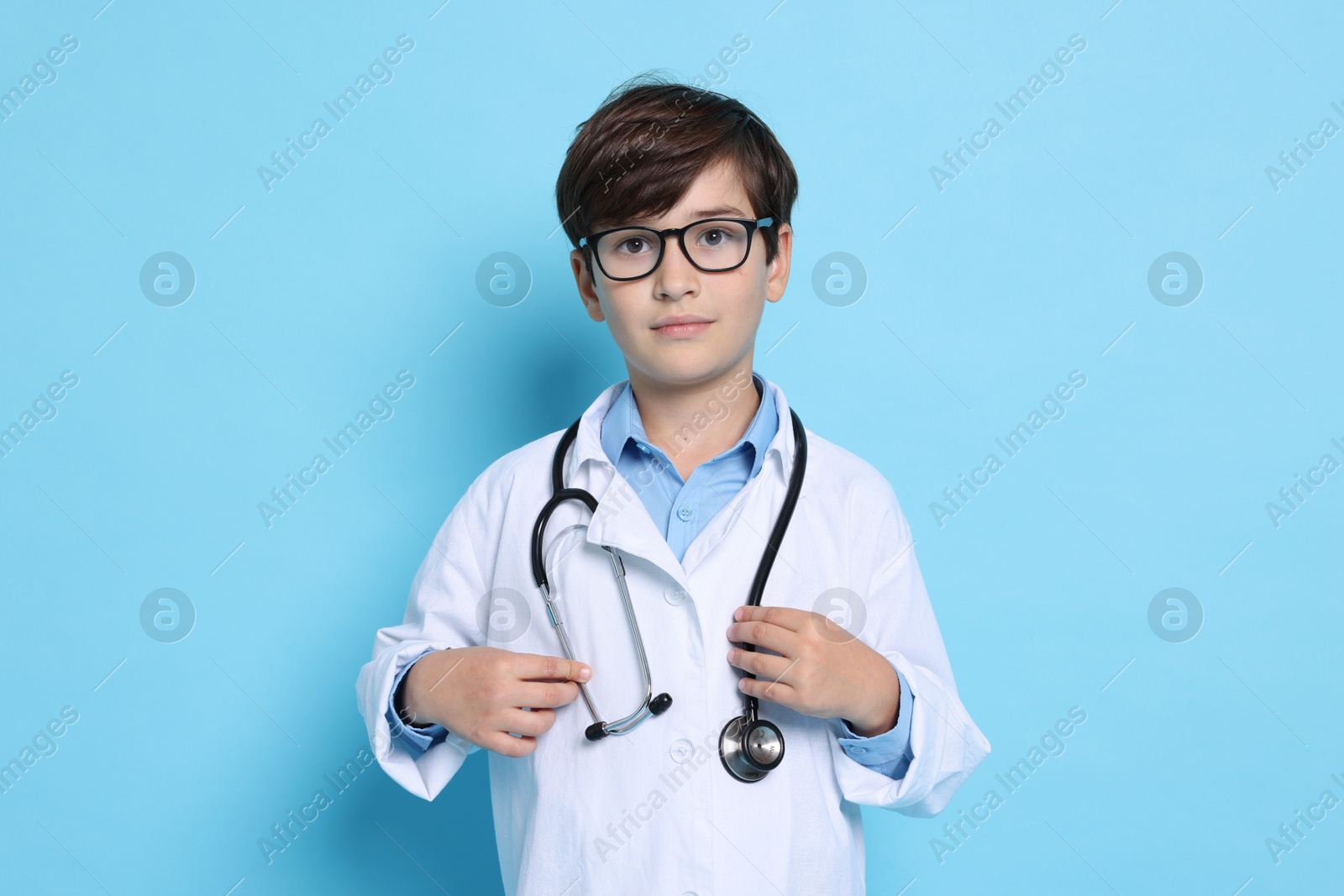 Photo of Boy with stethoscope pretending to be doctor on light blue background. Dreaming of future profession