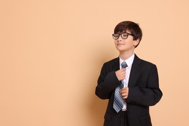 Boy in suit pretending to be businessman on beige background, space for text. Dreaming of future profession