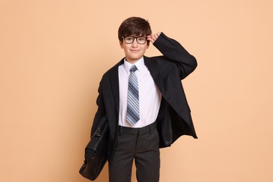 Boy in suit pretending to be businessman on beige background. Dreaming of future profession