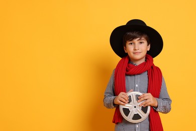 Photo of Boy with film reel pretending to be movie director on orange background, space for text. Dreaming of future profession