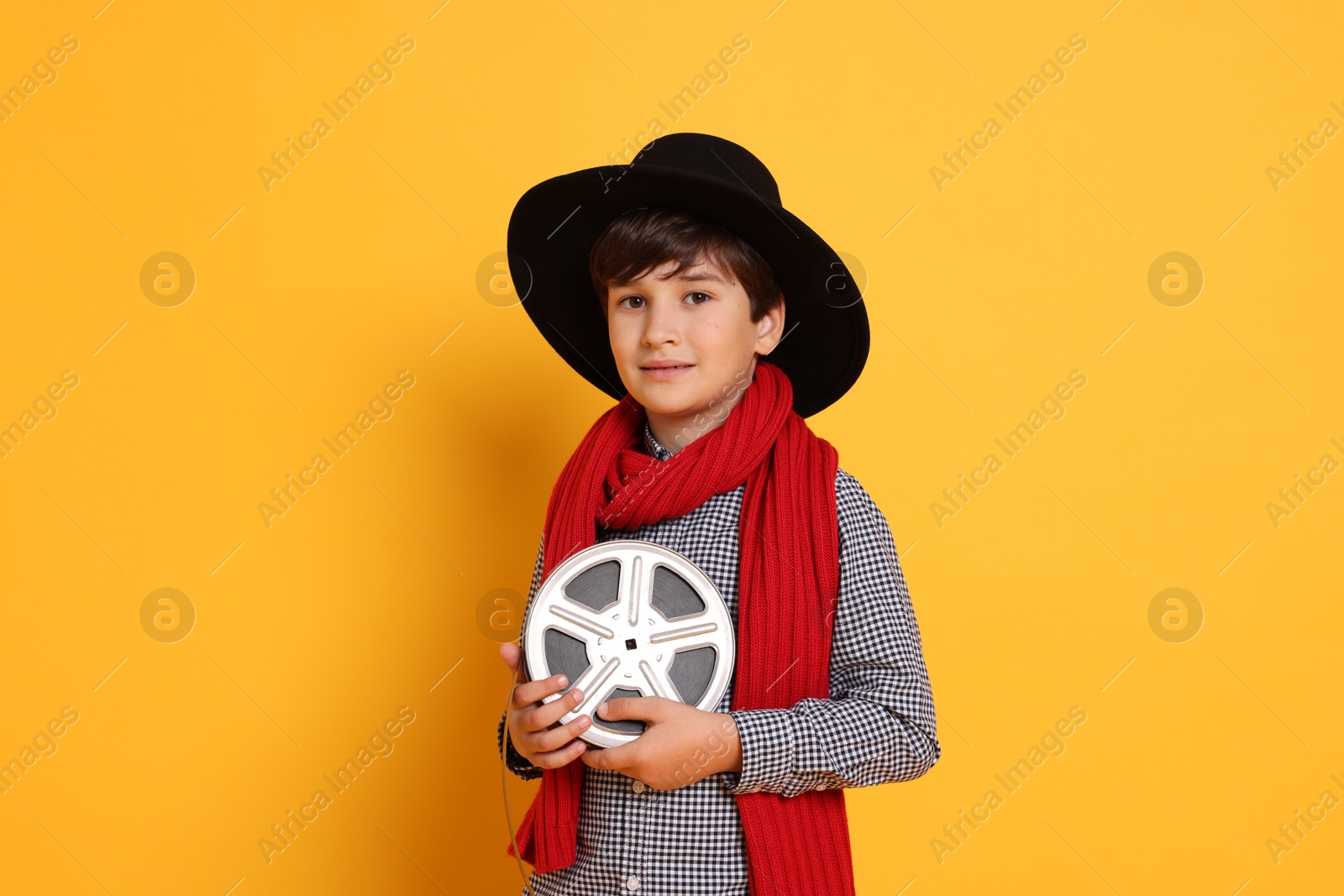 Photo of Boy with film reel pretending to be movie director on orange background. Dreaming of future profession