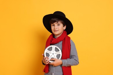 Photo of Boy with film reel pretending to be movie director on orange background. Dreaming of future profession