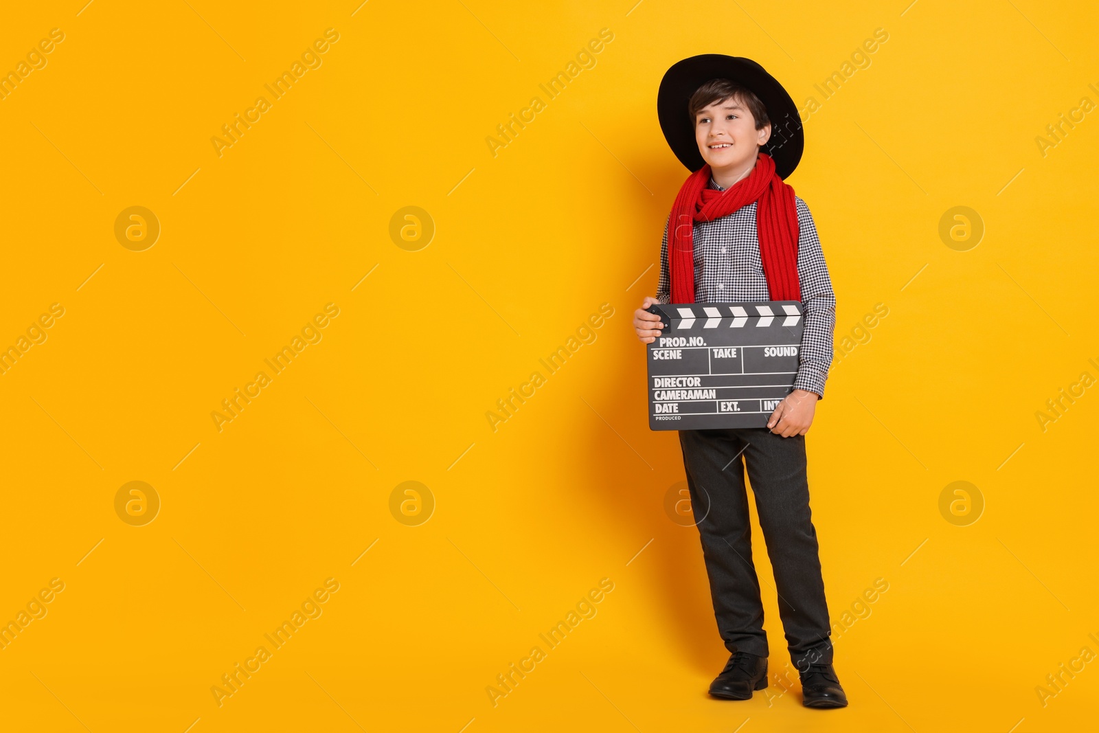 Photo of Boy with clapper pretending to be movie director on orange background, space for text. Dreaming of future profession