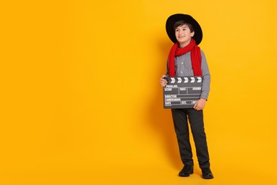 Boy with clapper pretending to be movie director on orange background, space for text. Dreaming of future profession