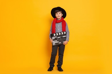 Photo of Boy with clapper pretending to be movie director on orange background. Dreaming of future profession