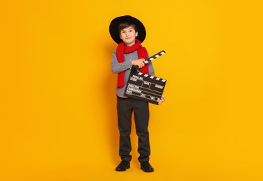 Photo of Boy with clapper pretending to be movie director on orange background. Dreaming of future profession