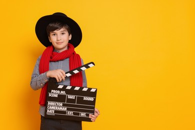 Boy with clapper pretending to be movie director on orange background, space for text. Dreaming of future profession