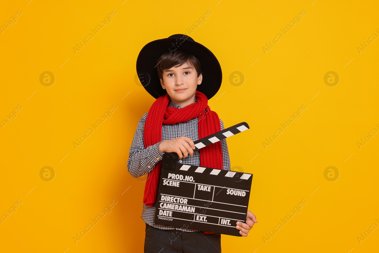 Photo of Boy with clapper pretending to be movie director on orange background. Dreaming of future profession