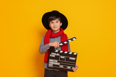 Boy with clapper pretending to be movie director on orange background. Dreaming of future profession