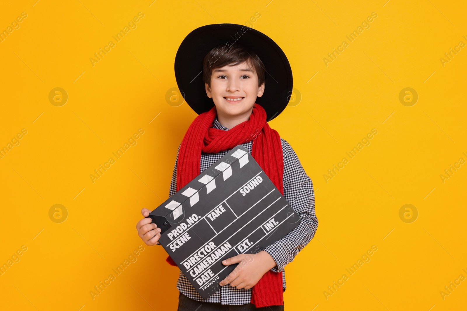 Photo of Boy with clapper pretending to be movie director on orange background. Dreaming of future profession