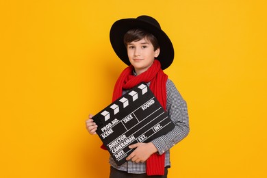 Photo of Boy with clapper pretending to be movie director on orange background. Dreaming of future profession