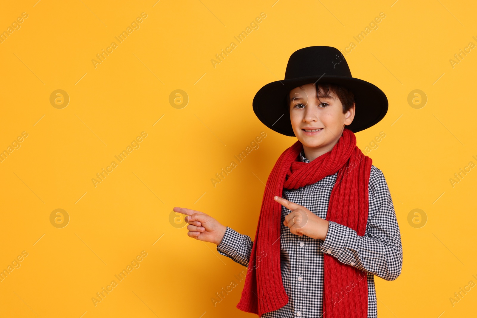 Photo of Boy with hat and scarf pointing at something on orange background, space for text. Dreaming of future profession