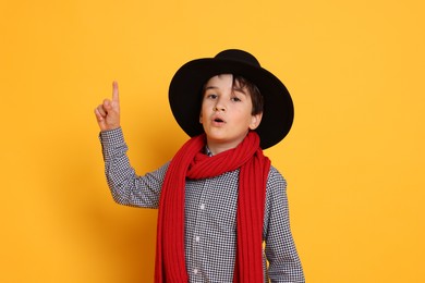 Photo of Boy with hat and scarf on orange background. Dreaming of future profession