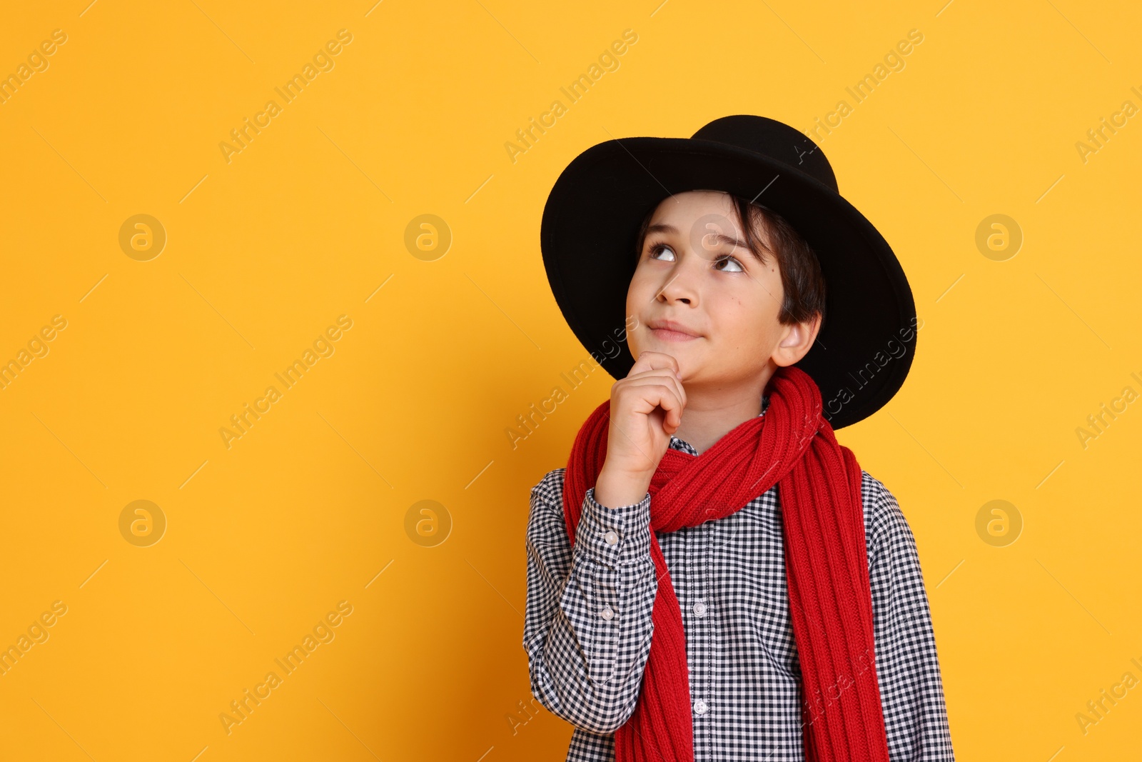 Photo of Boy with hat and scarf on orange background, space for text. Dreaming of future profession