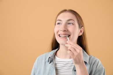 Photo of Girl with braces cleaning teeth with interdental brush on beige background, space for text