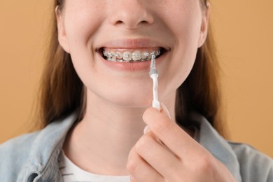 Photo of Girl with braces cleaning teeth with interdental brush on beige background, closeup