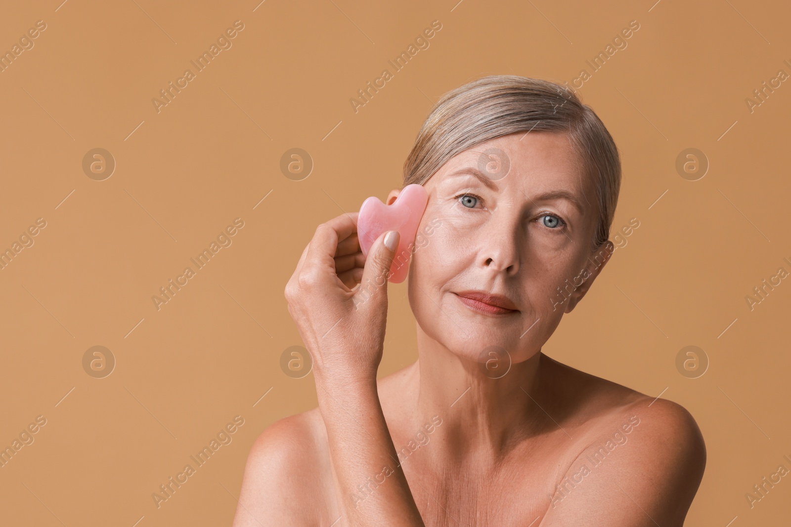 Photo of Beautiful woman doing facial massage with gua sha tool on beige background