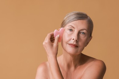 Beautiful woman doing facial massage with gua sha tool on beige background