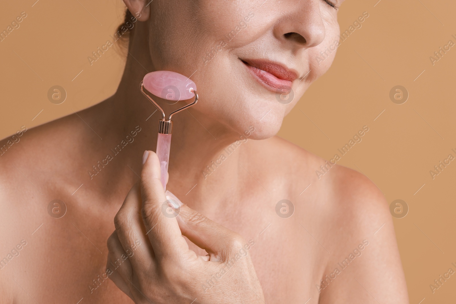 Photo of Woman doing facial massage with roller on beige background, closeup