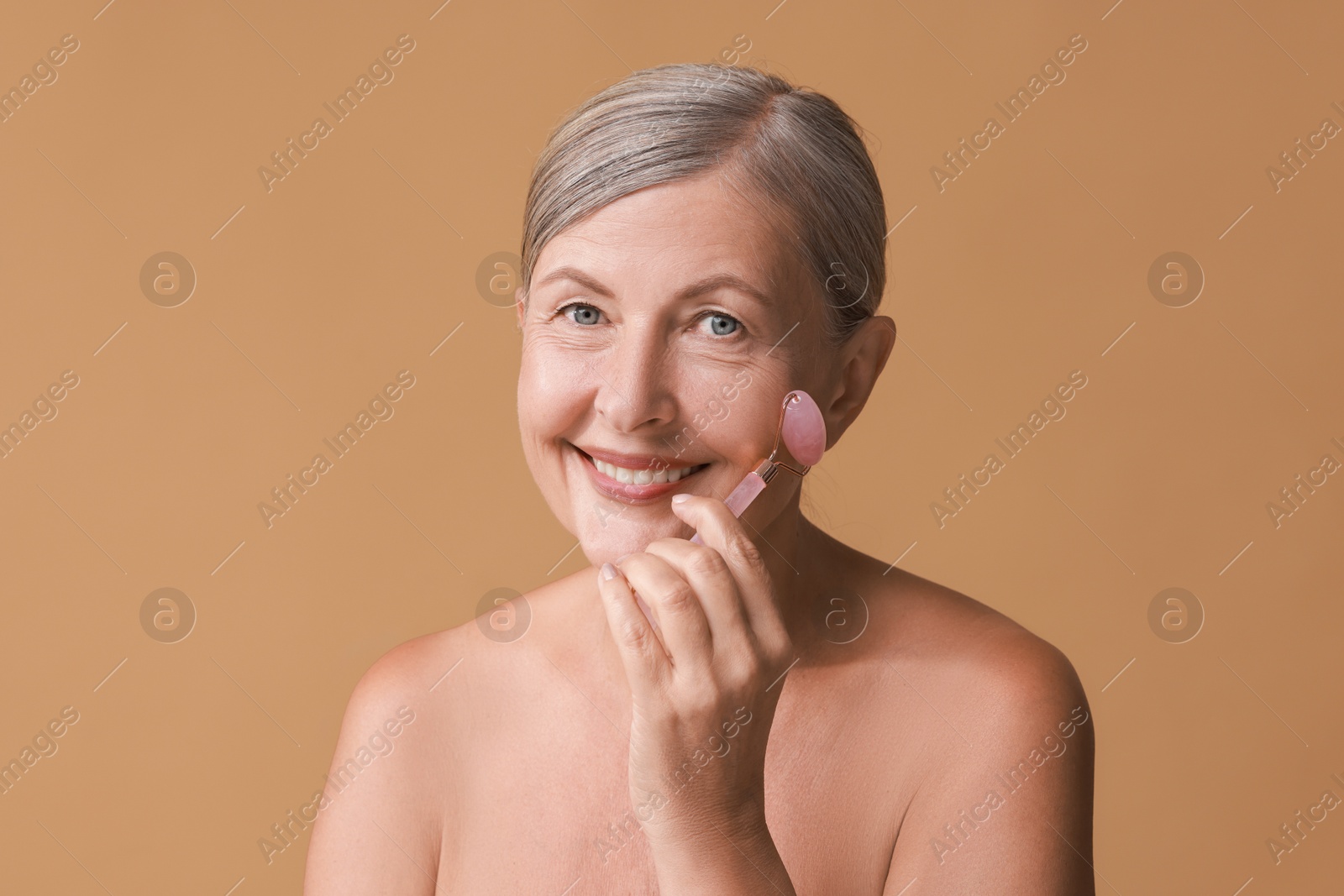 Photo of Beautiful woman doing facial massage with roller on beige background