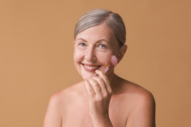 Beautiful woman doing facial massage with roller on beige background