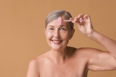 Beautiful woman doing facial massage with roller on beige background