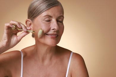 Photo of Beautiful woman doing facial massage with roller on beige background