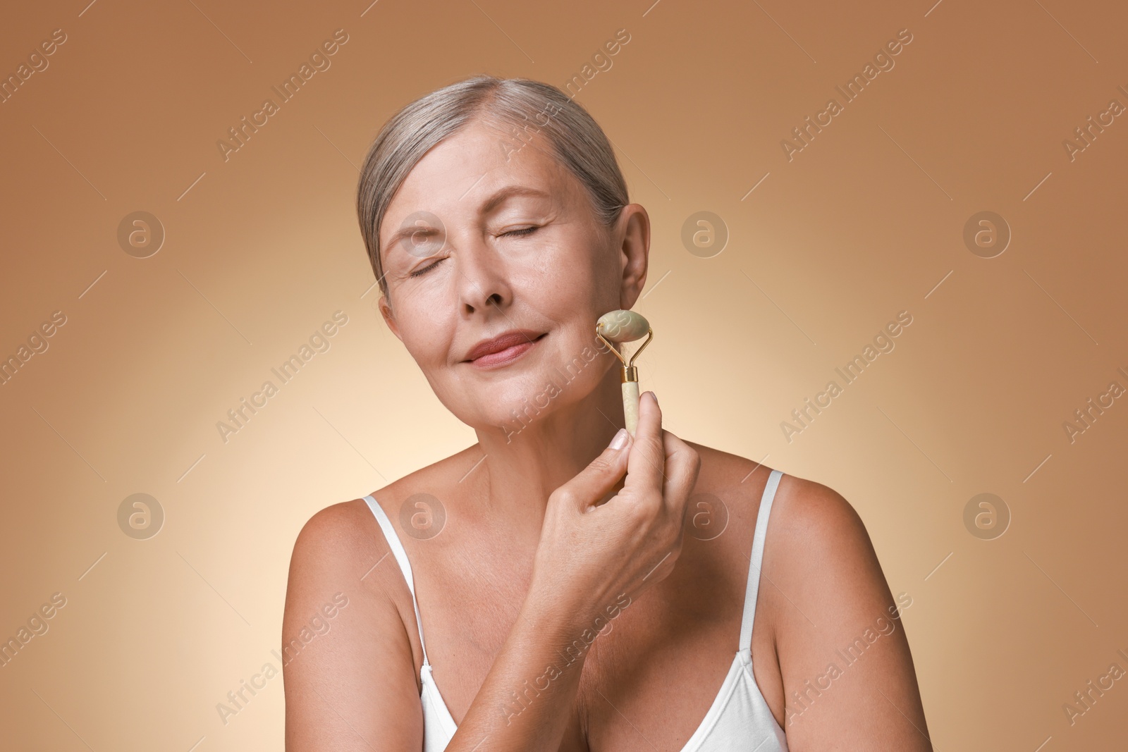 Photo of Beautiful woman doing facial massage with roller on beige background