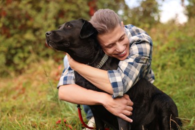 Smiling man hugging cute dog outdoors on autumn day